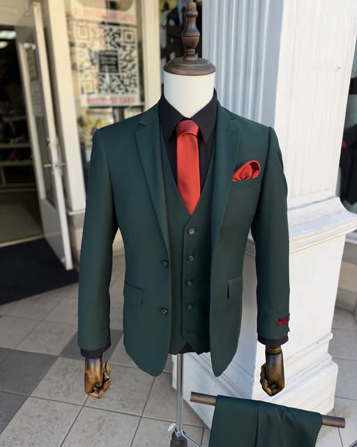 A forest-green three-piece suit with a red tie on a mannequin